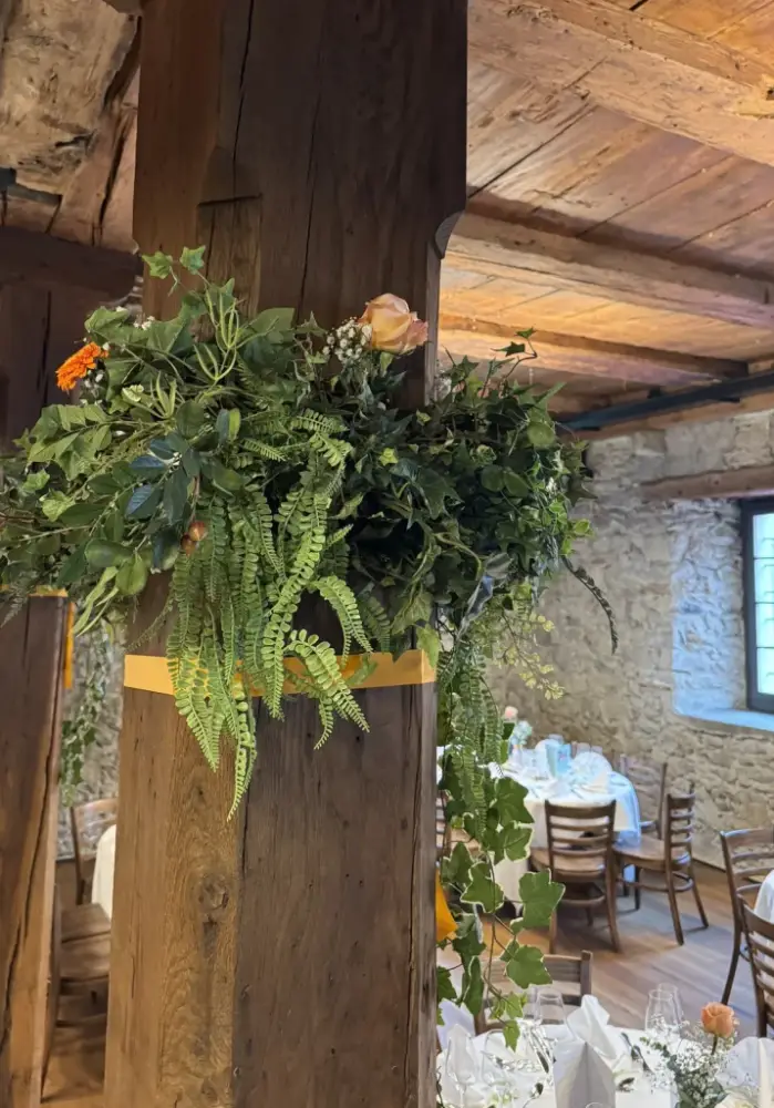 Grüner Blumenschmuck mit Farn, Efeu, Pfirsichrose und Gerbera an einer alten Holzsäule im Mühleraum