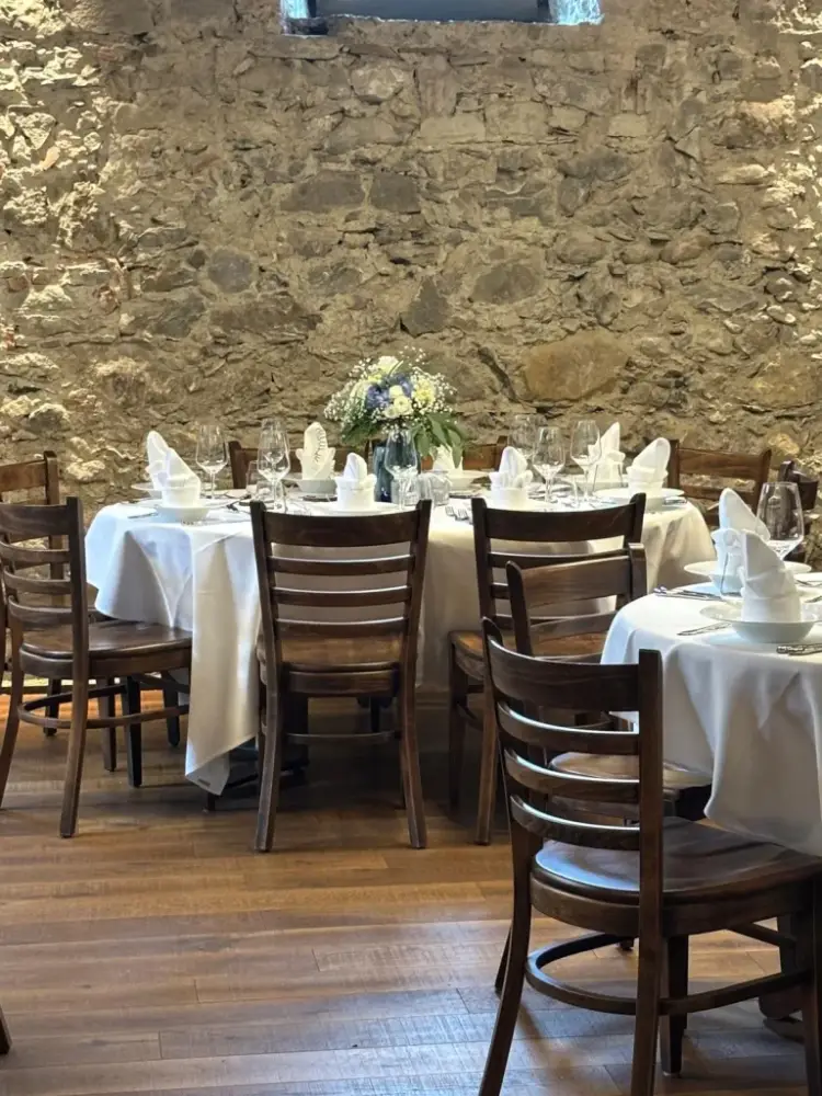 Runde Hochzeitstische mit weissen Tischtüchern, Holzstühlen und Blumen in Blau und Weiss vor der Natursteinmauer im Mühlerama Seon