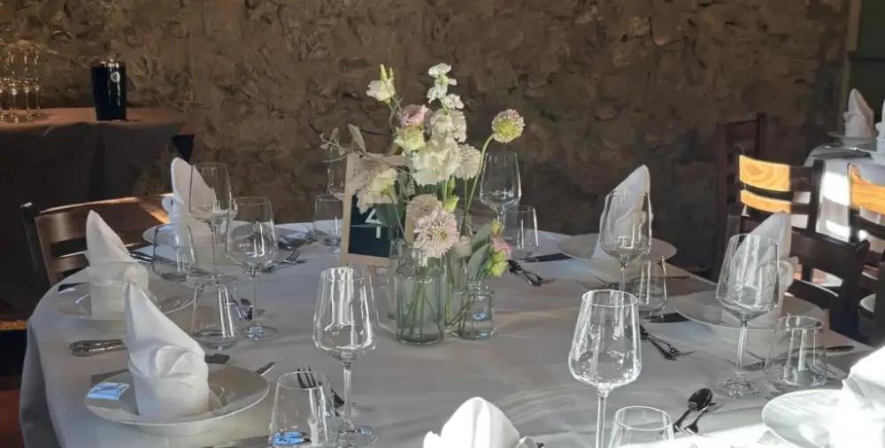 Hochzeitstisch im Sonnenlicht mit zarten Blumen in Glasvasen, Kristallgläsern und kunstvoll gefalteten Servietten